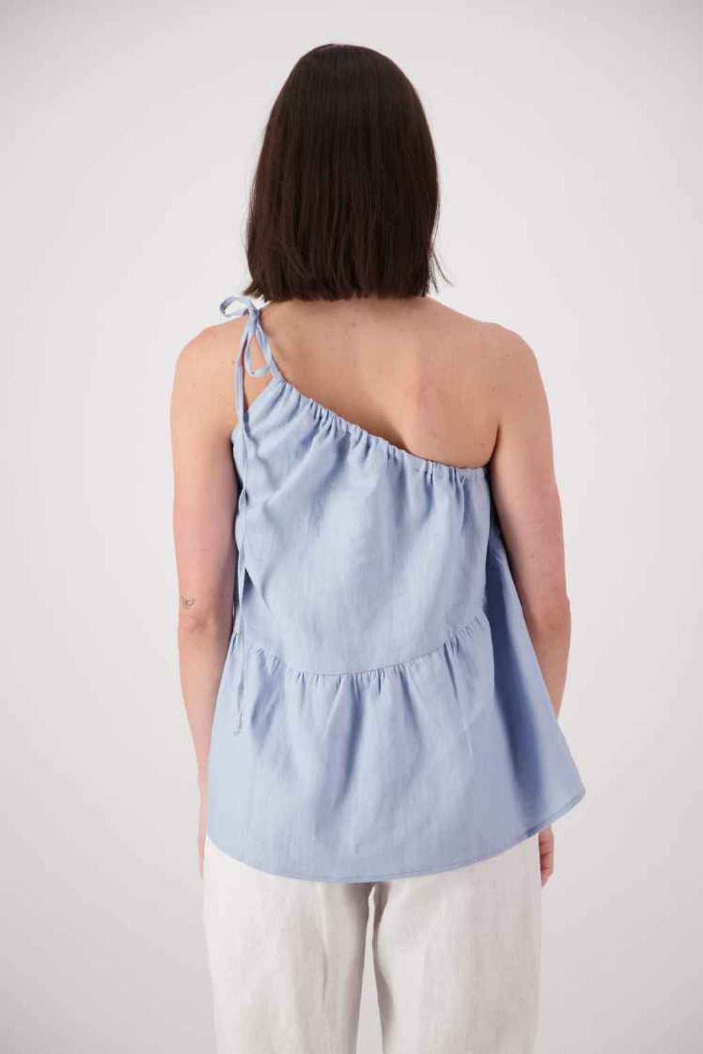 Back view sky blue: "Ranfurly linen top in sky blue back view showing single shoulder strap and relaxed frill hem, handmade by Lohi Linen in Ranfurly"