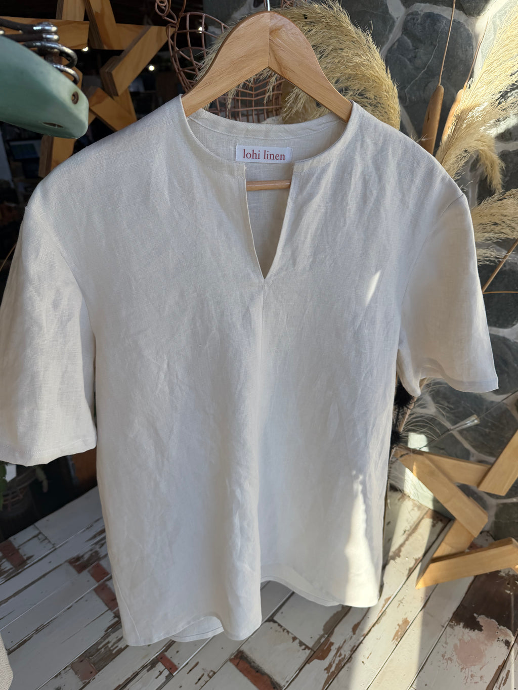 Shirt on hanger: "St Bathans linen t-shirt in Silvered Almond on hanger showing notch neckline detail, handmade by Lohi Linen in Central Otago, New Zealand