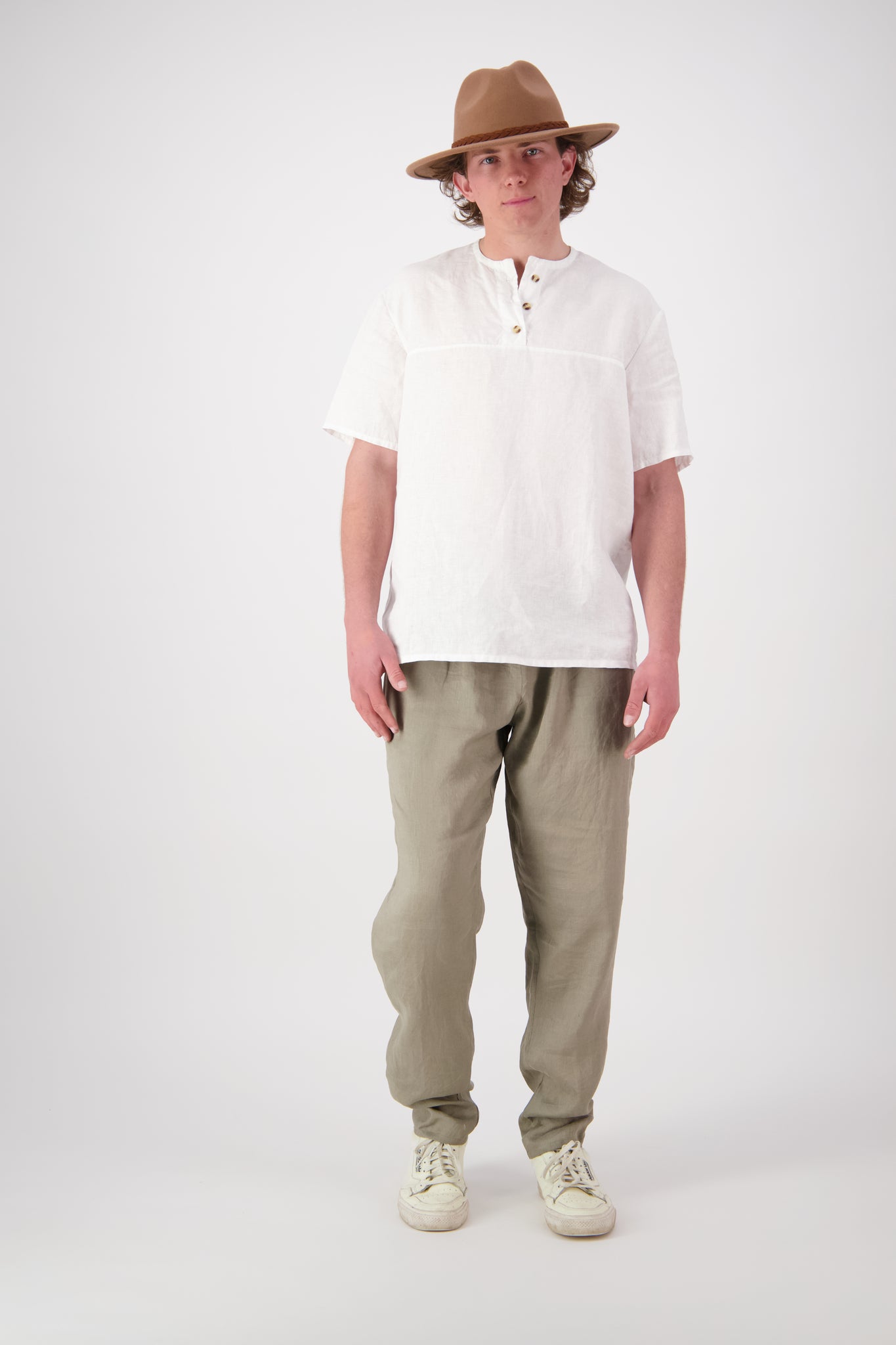 Front view white (stone): "Hawkdun linen top in stone worn with olive linen pants, relaxed henley short sleeve, handmade by Lohi Linen in Central Otago"